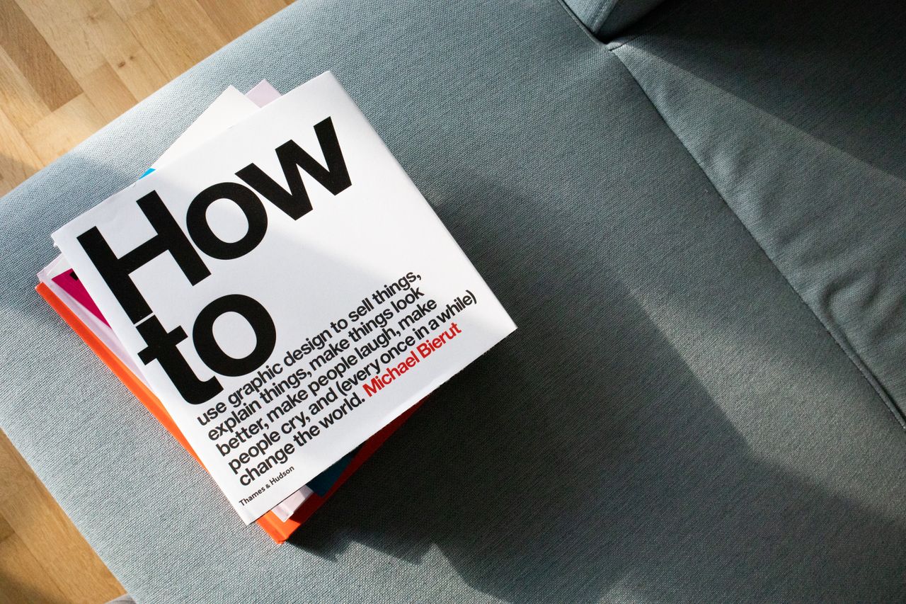 A collection of design books on a couch, showcasing How to by Michael Bierut